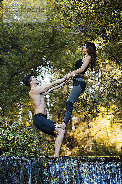 Ein Paar  das gemeinsam Akro-Yoga an einem Wasserfall praktiziert