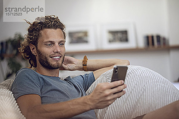 Lächelnder junger Mann entspannt sich im Sitzsack zu Hause am Handy
