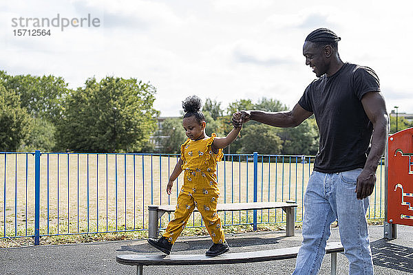 Vater hilft Tochter beim Balancieren auf einer Plattform auf einem Spielplatz