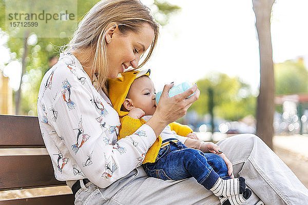 Mit der Flasche stillende Mutter eines Jungen auf einer Parkbank