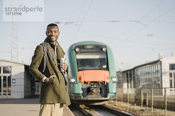 Porträt eines lächelnden Mannes mit wiederverwendbarem Becher  der auf den Zug wartet
