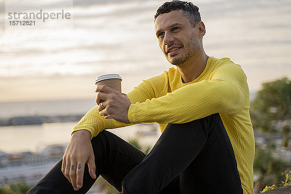 Mann sitzt bei Sonnenuntergang mit Kaffee zum Mitnehmen im Freien