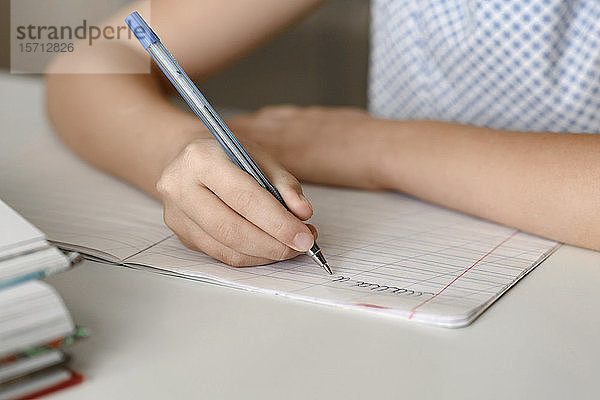 Nahaufnahme eines Mädchens  das zu Hause am Tisch sitzt und in ein Arbeitsbuch schreibt
