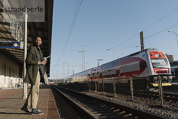 Stilvoller Mann mit wiederverwendbarem Becher wartet auf den Zug