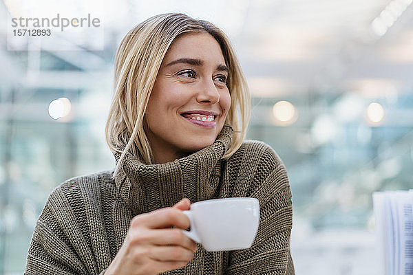 Porträt einer lächelnden jungen Frau  die eine Tasse Kaffee hält und wegschaut