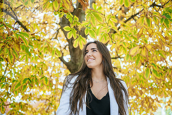 Lächelnde Frau steht unter herbstlichem Baum