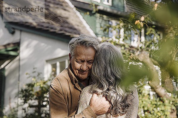 Älterer Mann umarmt seine Frau im Herbst im Garten ihres Hauses