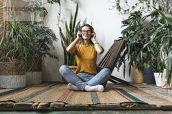 Entspannte junge Frau sitzt zu Hause auf dem Boden und hört Musik
