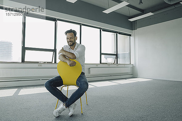 Porträt eines selbstbewussten reifen Geschäftsmannes auf gelbem Stuhl in einem leeren Büro