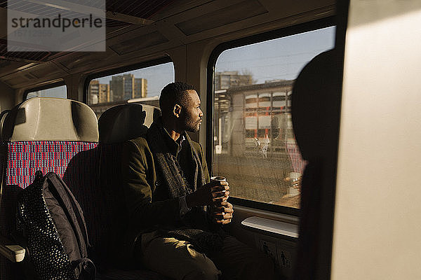 Stilvoller Mann mit wiederverwendbarem Becher in einem Zug