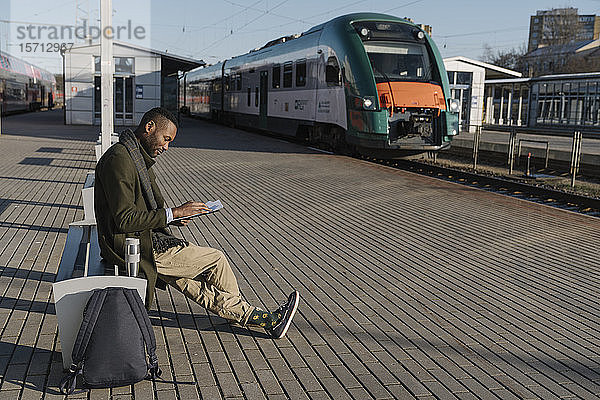Stilvoller Mann liest Dokumente beim Warten auf den Zug