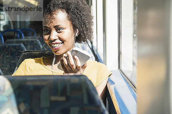 Glückliche junge Frau mit Kopfhörern und Smartphone im Zug