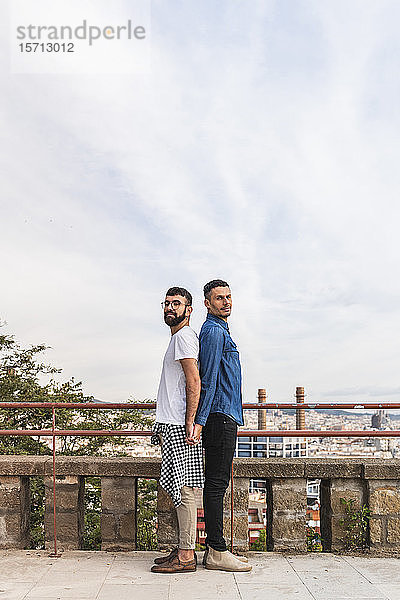 Porträt eines schwulen Paares  das Rücken an Rücken steht und sich an den Händen hält  Barcelona  Spanien