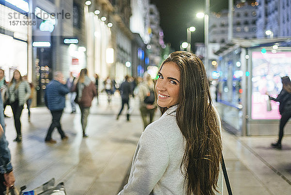Porträt einer lächelnden Frau  die nachts die Einkaufsstraße entlanggeht