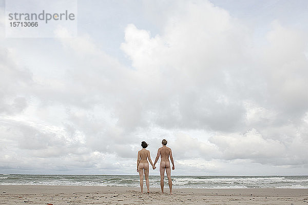 Am Strand stehendes  sich an den Händen haltendes  nacktes Paar