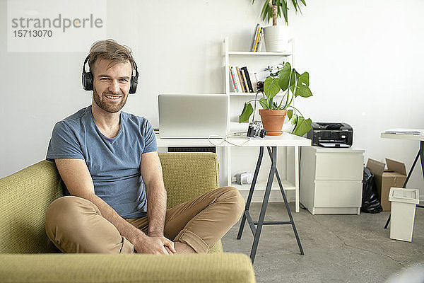 Porträt eines lächelnden Mannes  der im Büro auf der Couch sitzt und Musik hört