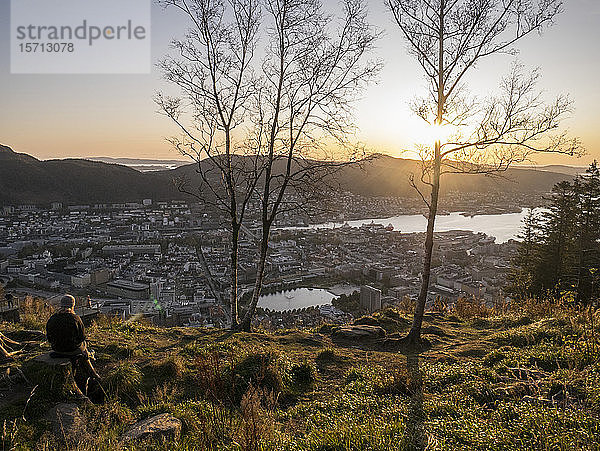 Norwegen  Bergen  Person  die den Sonnenuntergang vom Gipfel eines Hügels mit Blick auf die Küstenstadt bewundert