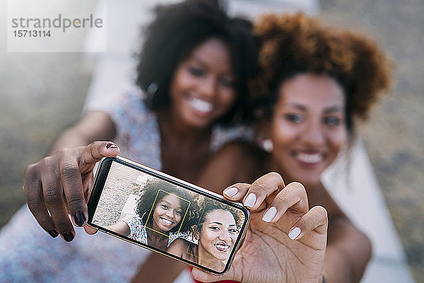 Junge Frauen  die lächeln und sich mit ihrem Smartphone in einem Park ein Selfie machen