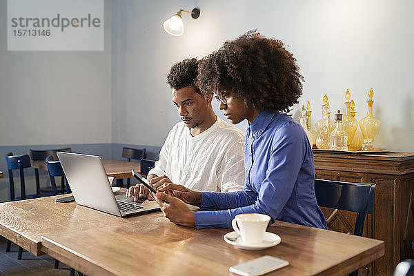 Schülerinnen und Schüler  die Laptop und Tablet für ein Projekt in einem Café benutzen