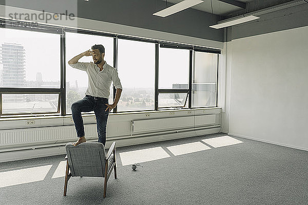 Reifer Geschäftsmann steht auf Sessel in leerem Büro