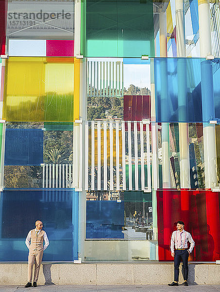 Zwei elegante Männer stehen an einem Gebäude mit farbenfroher Fassade