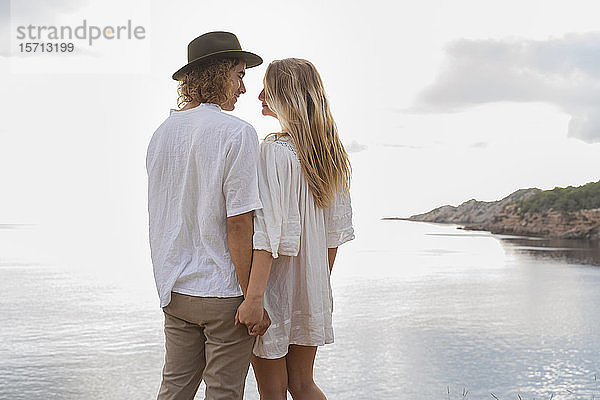 Verliebtes junges Paar  das vor dem Meer steht und Händchen hält  Ibiza  Balearen  Spanien