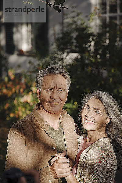 Porträt eines glücklichen älteren Ehepaares im Herbst im Garten ihres Hauses