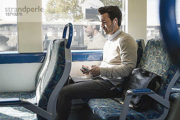 Junger Mann mit Kopfhörern mit Smartphone und Tablet in einem Zug