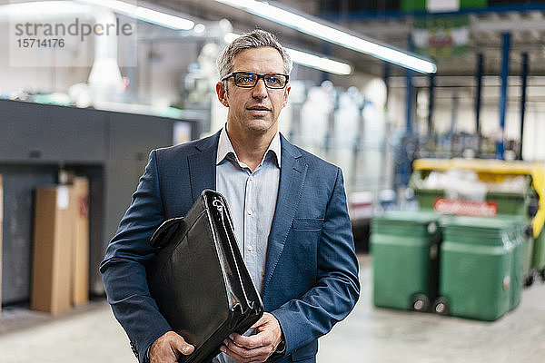 Porträt eines Geschäftsmannes mit Brille und Aktentasche in einer Fabrik