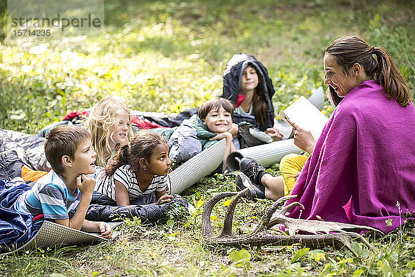 Lehrer liest Schulkindern eine Geschichte vor  Camping im Wald
