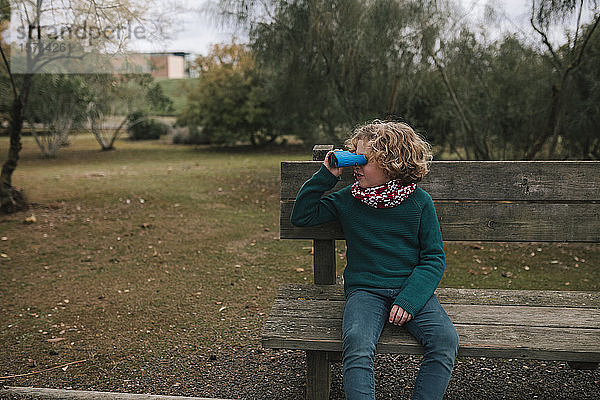 Junge  der im Herbst auf einer Bank sitzt und etwas mit dem Fernglas beobachtet