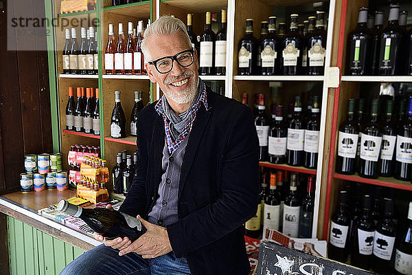 Porträt eines lächelnden reifen Mannes bei der Auswahl einer Flasche Wein in einem Weinladen