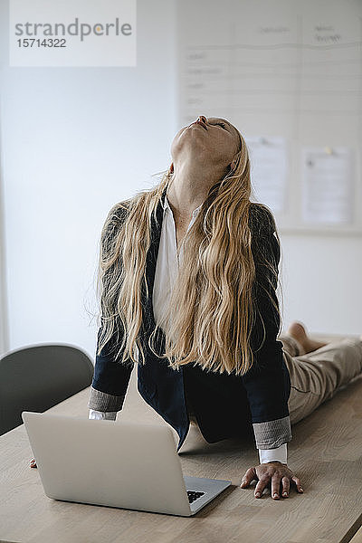 Junge Geschäftsfrau praktiziert Yoga auf dem Schreibtisch im Büro