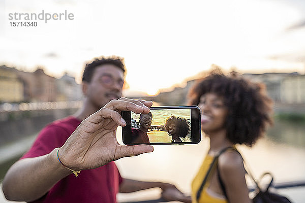 Junges Touristenpaar beim Selfie auf einer Brücke über den Arno bei Sonnenuntergang  Florenz  Italien