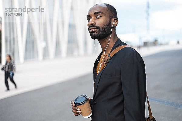 Porträt eines jungen Geschäftsmannes mit Kaffee zum Musikhören mit Kopfhörern im Freien