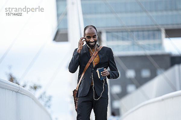 Lächelnder junger Geschäftsmann benutzt Smartphone und Kopfhörer im Freien