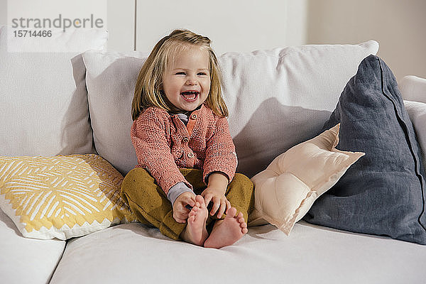 Lachendes kleines Mädchen sitzt zu Hause auf dem Sofa