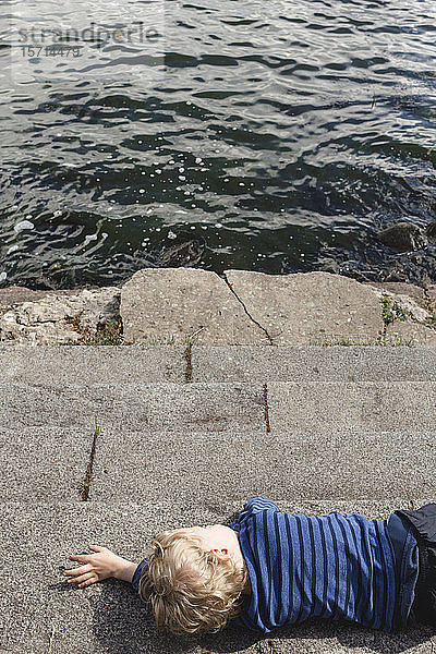 Kleiner Junge ruht sich am Seeufer aus