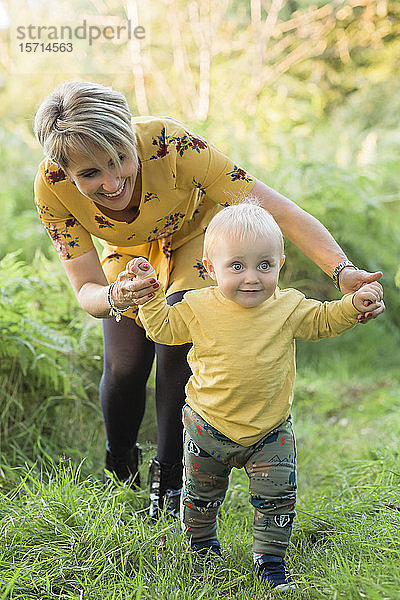 Mutter hilft kleinem Sohn beim Spaziergang auf einer Wiese