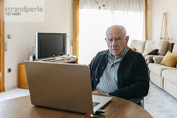 Portrait eines zufriedenen Seniormanns im Rollstuhl mit Laptop zu Hause