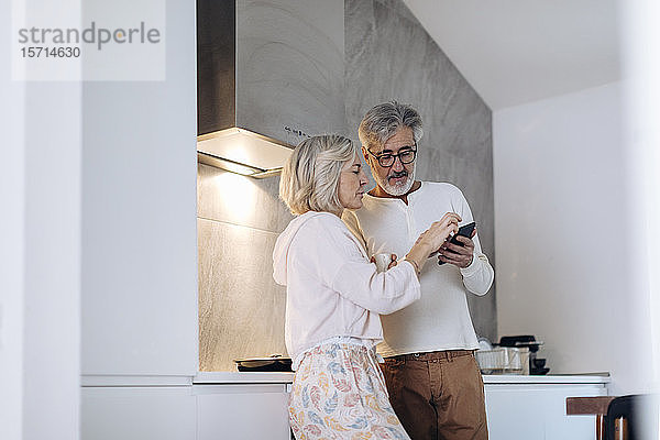 Ein erwachsenes Paar benutzt zu Hause in der Küche ein Mobiltelefon