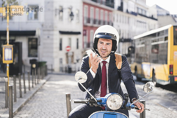 Junger Geschäftsmann mit Motorroller mit Mobiltelefon in der Stadt  Lissabon  Portugal