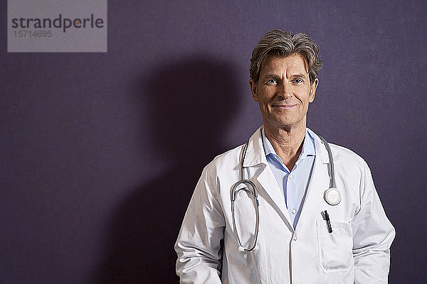 Porträt eines selbstbewussten Arztes vor einer violetten Wand