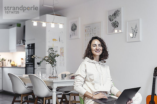 Porträt einer lächelnden Frau mit Laptop zu Hause