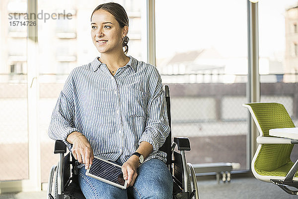 Junge Geschäftsfrau mit Tablett im Rollstuhl sitzend im Büro
