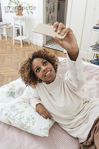 Glückliche junge Frau  die im Bett liegt und ein Selfie