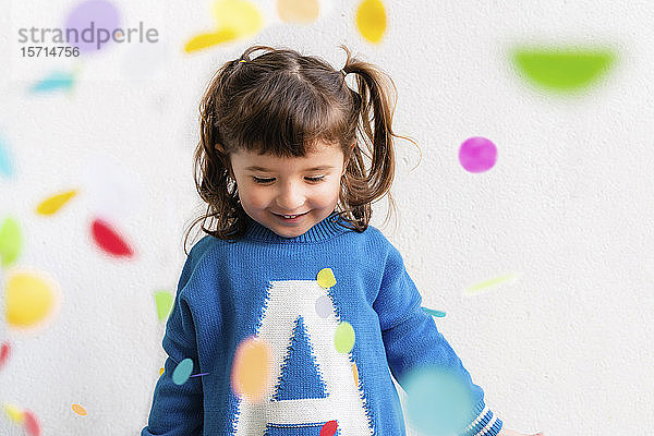 Glückliches kleines Mädchen mit dem Konfetti während einer Party vor einer weißen Wand