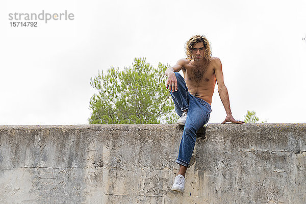 Junger blonder Mann sitzt auf einer Mauer