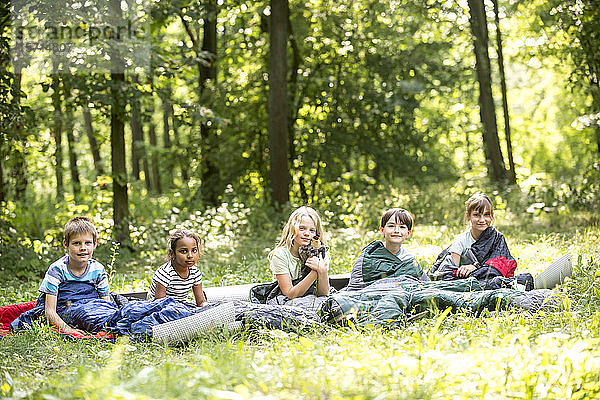 Kinder  die im Wald zelten und in ihren Schlafsäcken sitzen