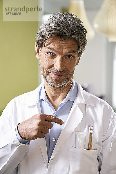 Porträt eines Zahnarztes  der auf eine Zahnbürste in seiner Tasche zeigt